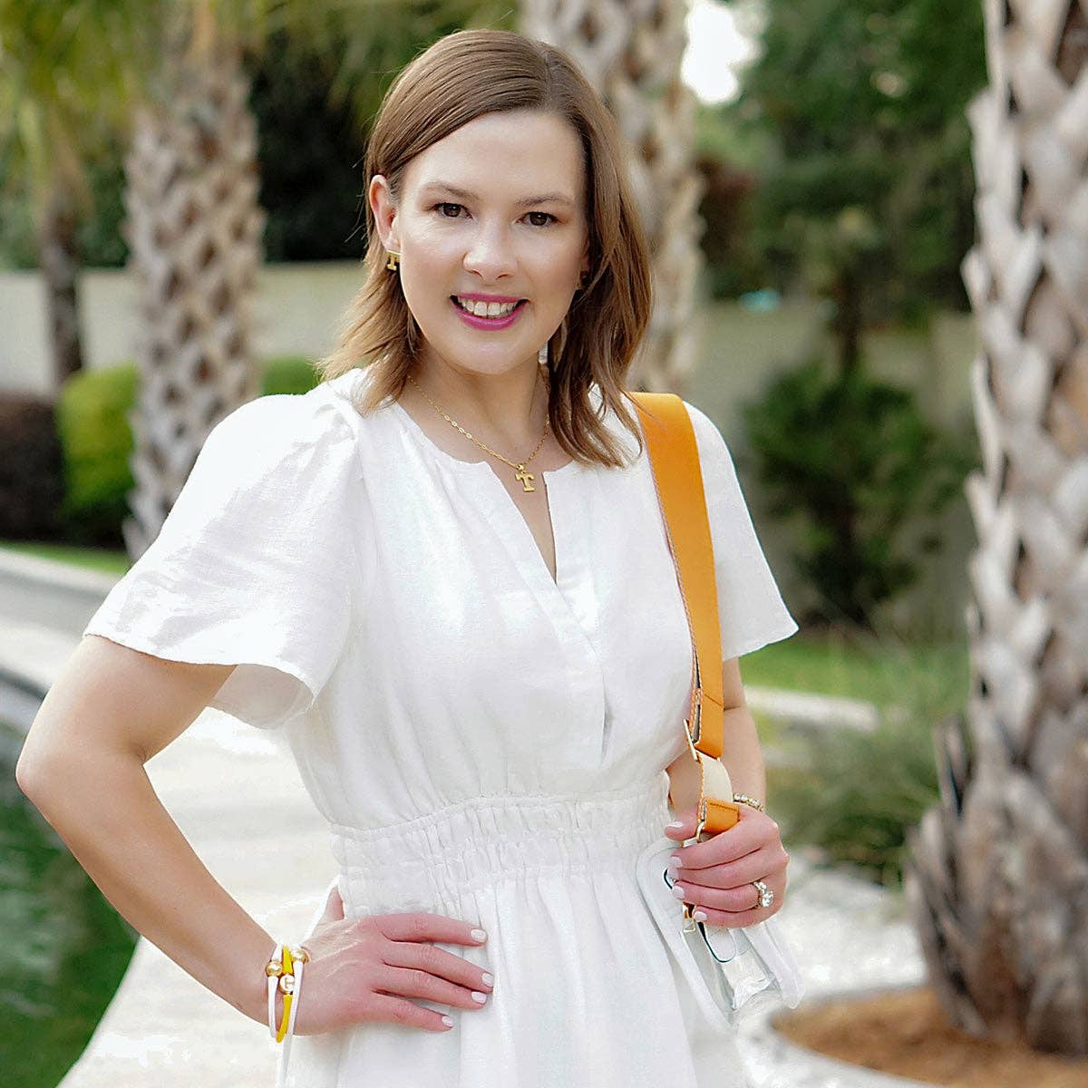 Woman in a white dress with a yellow strap posing outdoors.