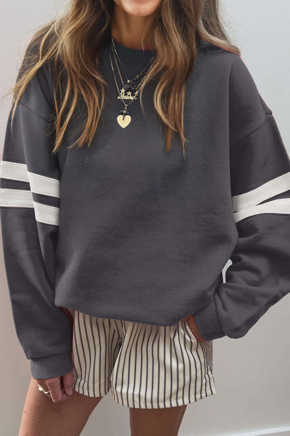 Woman wearing a dark grey oversized sweatshirt with white varsity sleeve stripes and striped shorts — sporty casual style from The Pink Doxie.