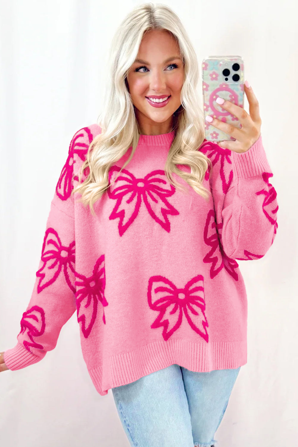 Woman wearing a pink sweater with large bows, holding a phone with a matching case.
