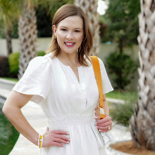 Woman in a white dress with a yellow strap posing outdoors.
