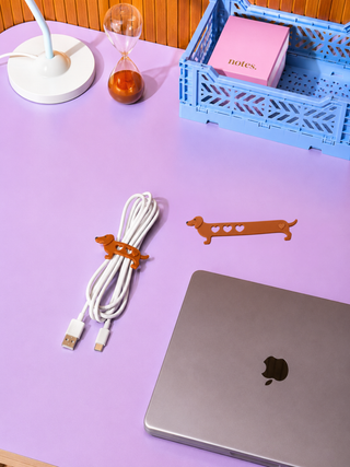 Brown dachshund-shaped cable ties with heart cutouts, one securing white cables on a desk.