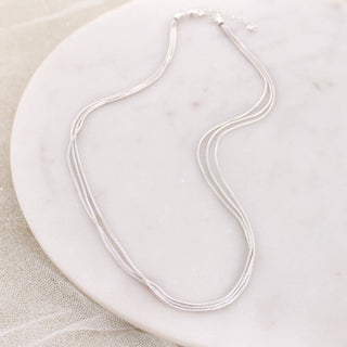 Silver three-strand snake chain necklace displayed on a white marble background.