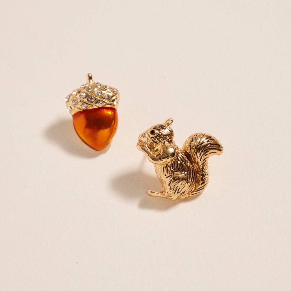 Mismatched fall earrings featuring a gold squirrel stud and jeweled acorn stud displayed on a neutral background