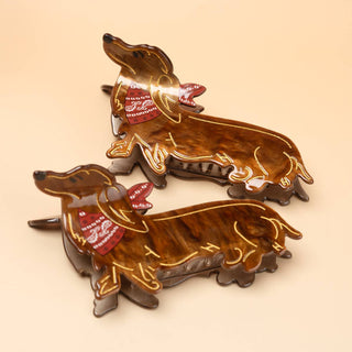 Dachshund-shaped hair claw clip with a tortoiseshell base, gold line art, and red bandana.