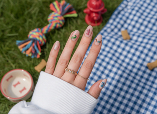 Hand with Weenie Dog Nail Stickers featuring playful puppy designs in a garden setting.