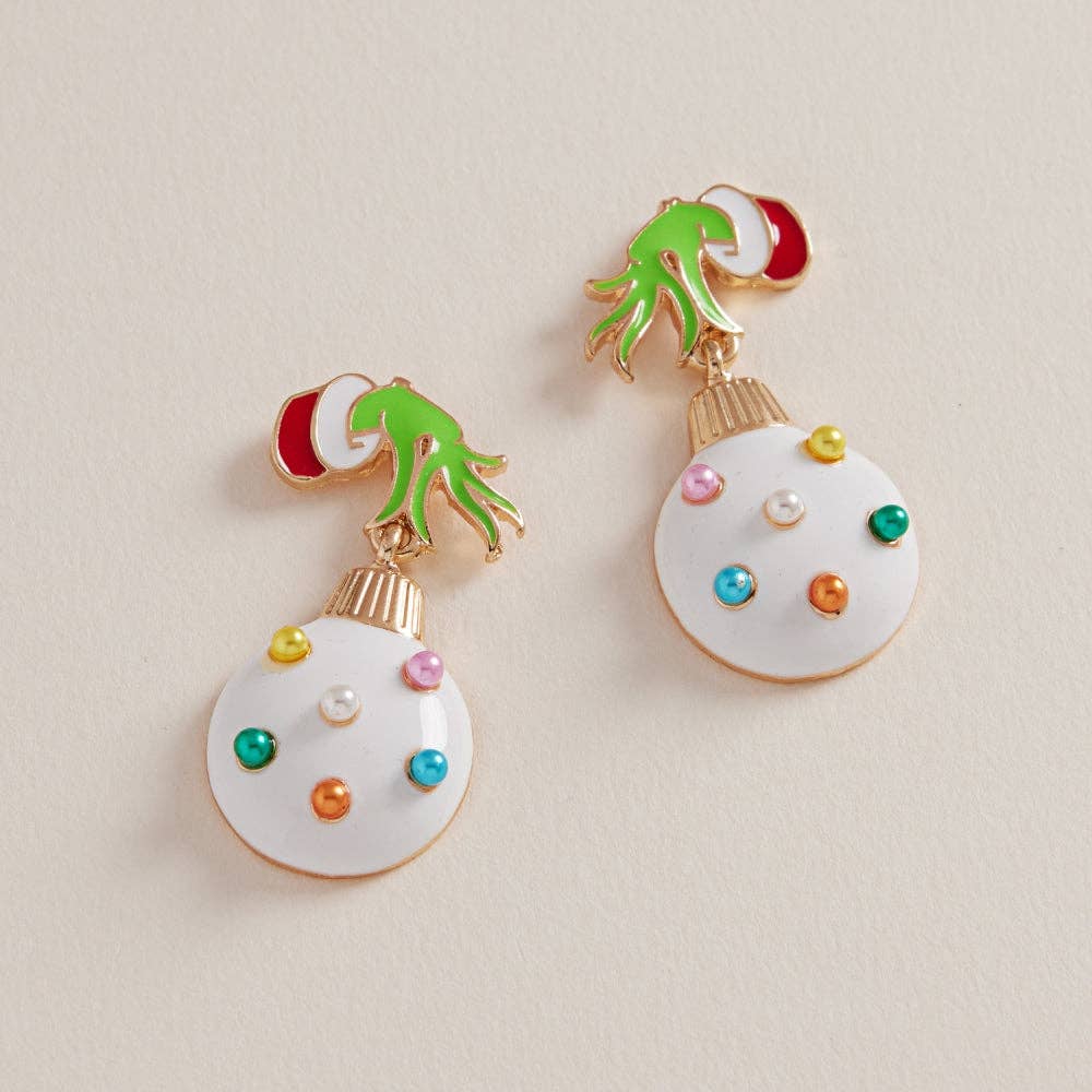 Whimsical earrings featuring a green holiday hand holding a pearl-studded white ornament with colorful accents on a neutral background.