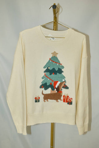 Cream long sleeve sweater with a dachshund wearing a Santa hat, standing next to a decorated Christmas tree and gifts.