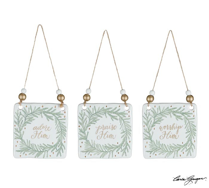 Three hand-painted ceramic square ornaments with greenery wreaths and gold lettering reading Adore Him, Praise Him, and Worship Him — faith-inspired Christmas décor from The Pink Doxie.