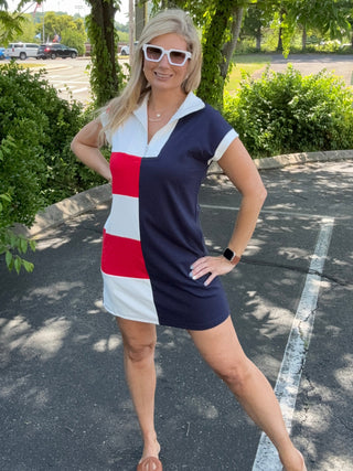 Woman in a red, white, and blue dress standing outdoors with trees and pavement in the background
