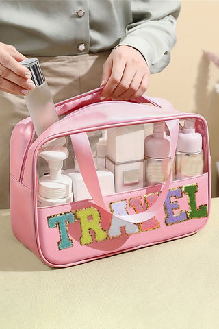 Light pink clear PVC makeup bag with chenille TRAVEL lettering and top handles, filled with beauty products, from The Pink Doxie Boutique.