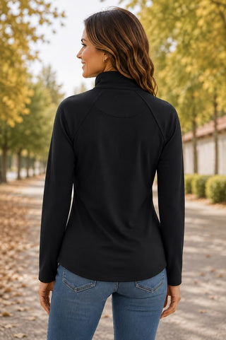 A woman wearing a fitted solid black long-sleeve quarter-zip pullover with a mock collar, raglan sleeves, and side hand pockets, styled with blue jeans.