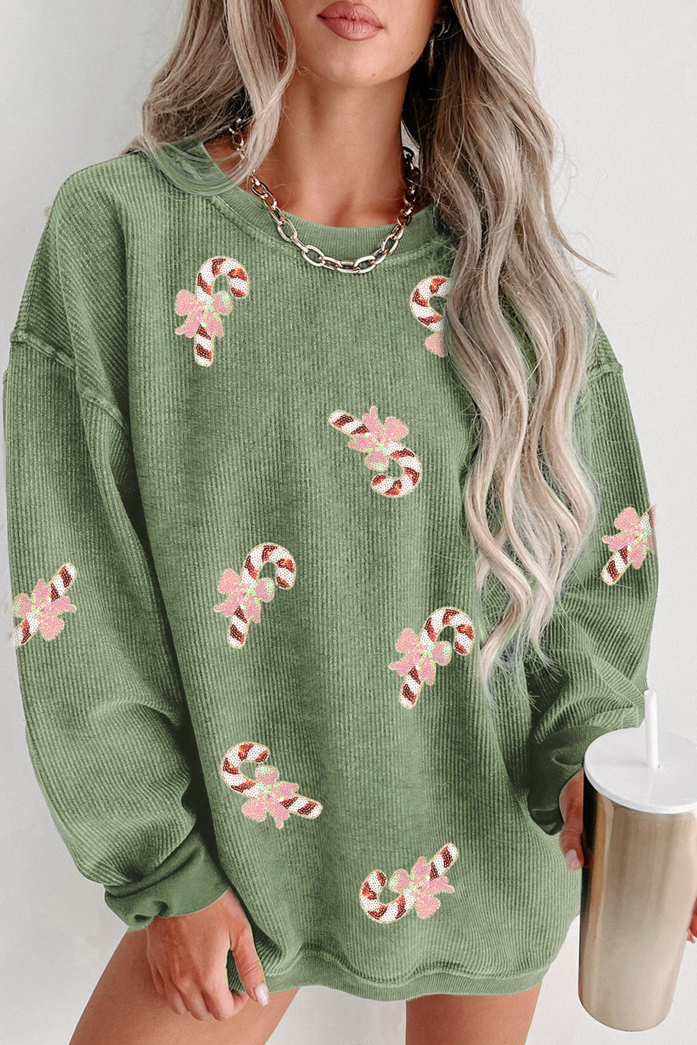 Woman wearing an oversized green ribbed sweatshirt with pink sequin candy cane patches — festive holiday pullover from The Pink Doxie.