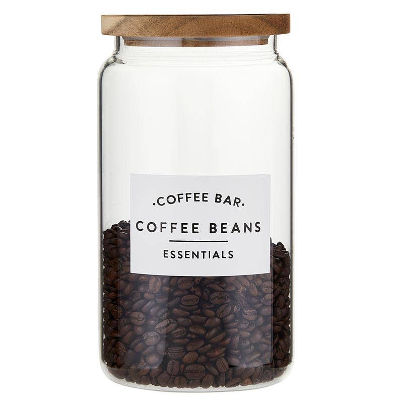 Glass coffee canister with acacia wood lid labeled “Coffee Bar Essentials” filled with coffee beans — kitchen storage jar from The Pink Doxie Boutique.