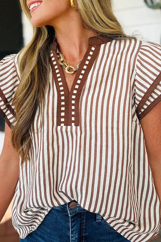 Woman wearing a khaki striped blouse with ruffled sleeves and a V-neckline styled with denim from The Pink Doxie Boutique.