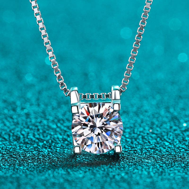Dainty moissanite pendant necklace in sterling silver with platinum finish — round solitaire design sparkling on teal background.