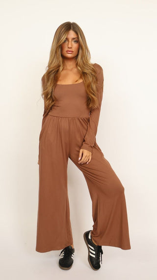 Woman wearing a tan Emma Jumpsuit with scoop neckline, long sleeves, and wide-leg silhouette, styled for effortless comfort from The Pink Doxie Boutique.