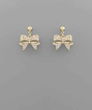 Gold-tone ribbon bow dangle earrings with cubic zirconia accents on a gray background from The Pink Doxie Boutique.