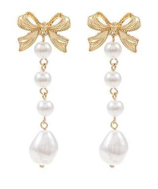 Gold bow drop earrings with linked faux pearl accents on a white background from The Pink Doxie Boutique.