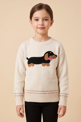A girl wearing a cream fine gauge knit crew neck pullover sweater with a textured black and tan dachshund appliqué on the front and ribbed cuffs and hem.