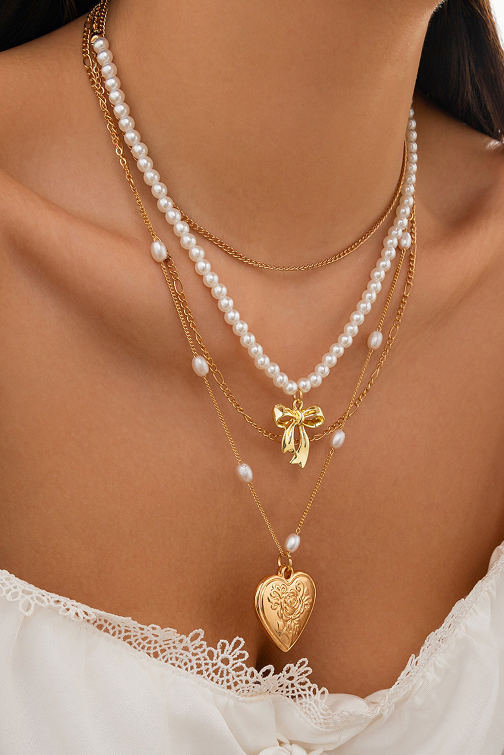 Gold layered necklace with pearls, gold bow charm, and engraved heart pendant displayed on white bust — elegant jewelry from The Pink Doxie Boutique
