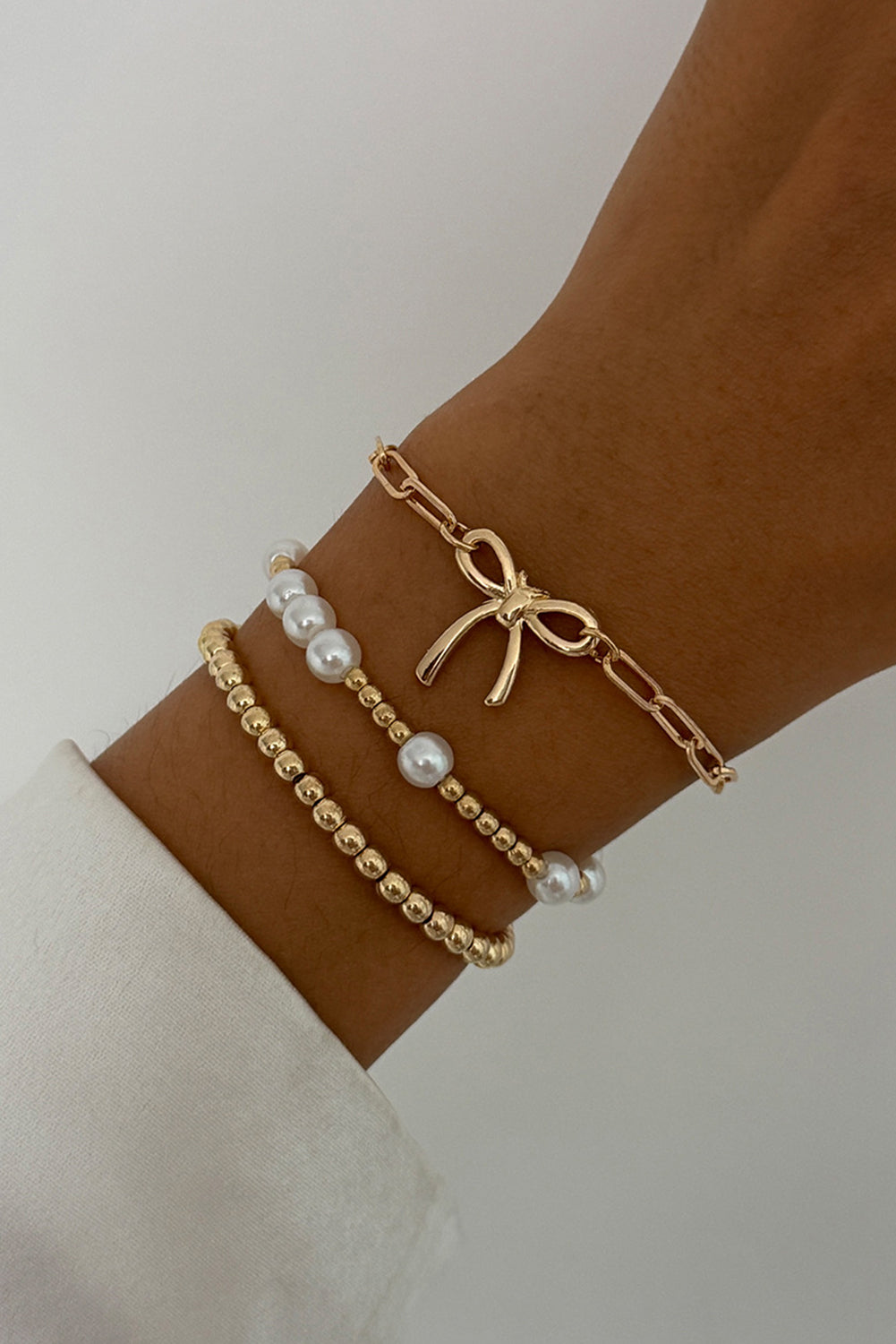Gold bow and pearl beaded bracelet trio stacked on wrist — elegant feminine jewelry set from The Pink Doxie Boutique.
