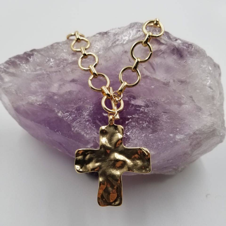 Gold hammered cross toggle necklace displayed on amethyst stone — faith-inspired fashion jewelry.