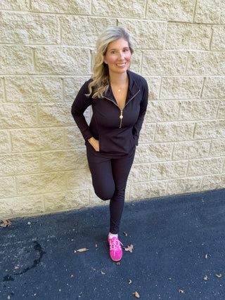 A woman wearing slim, fitted full-length black pull-on pants with a smooth, structured appearance, styled with a black quarter-zip pullover and pink sneakers.