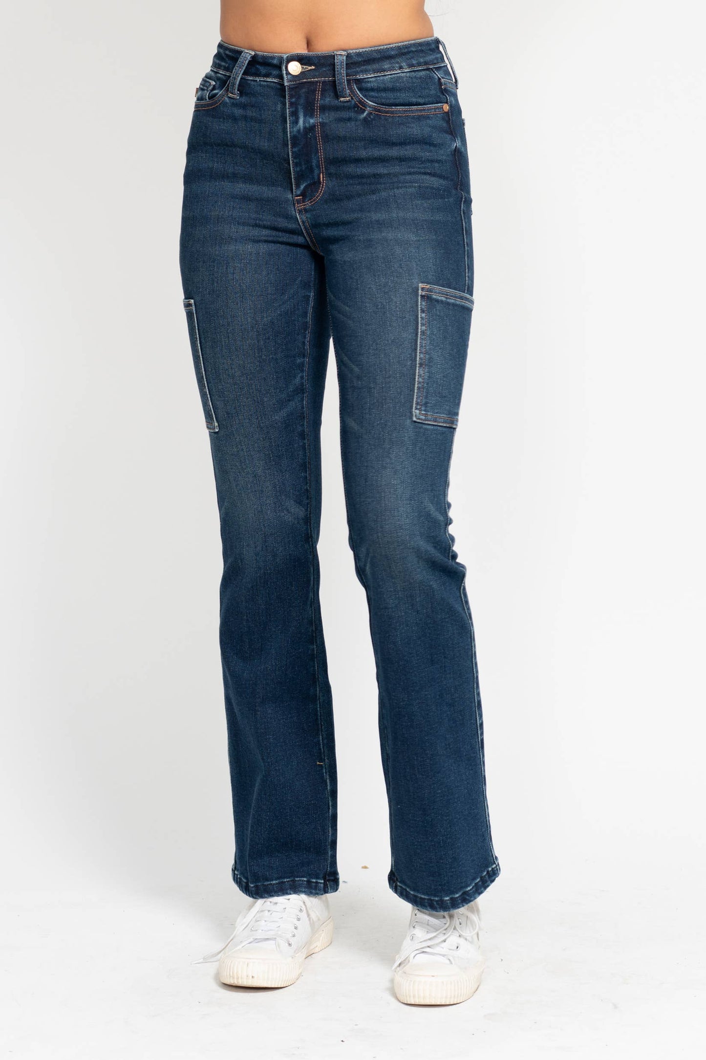 Model wearing Judy Blue High Waisted Cargo Bootcut Jeans in dark wash with utility-style pockets and white sneakers.
