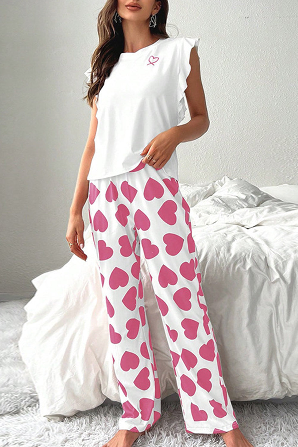 Woman wearing a white tank with ruffled sleeves and pink heart print lounge pants from The Pink Doxie.