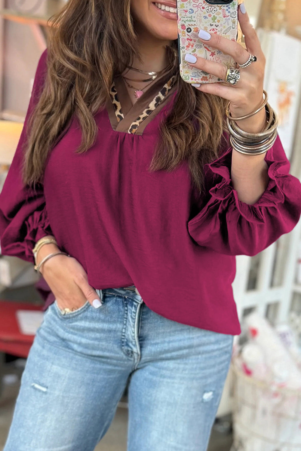 Woman wearing a violet V-neck blouse with leopard trim and flounced bracelet sleeves, paired with light wash jeans.