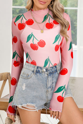 Woman wearing a pink cherry print sheer mesh top with long sleeves and mock neck
