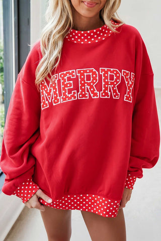An oversized red mock neck sweatshirt with a bold "MERRY" graphic in polka dot lettering and white polka dot contrast trim at the neckline, cuffs, and hem.