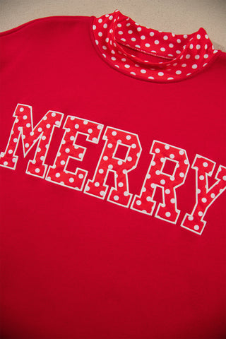An oversized red mock neck sweatshirt with a bold "MERRY" graphic in polka dot lettering and white polka dot contrast trim at the neckline, cuffs, and hem.