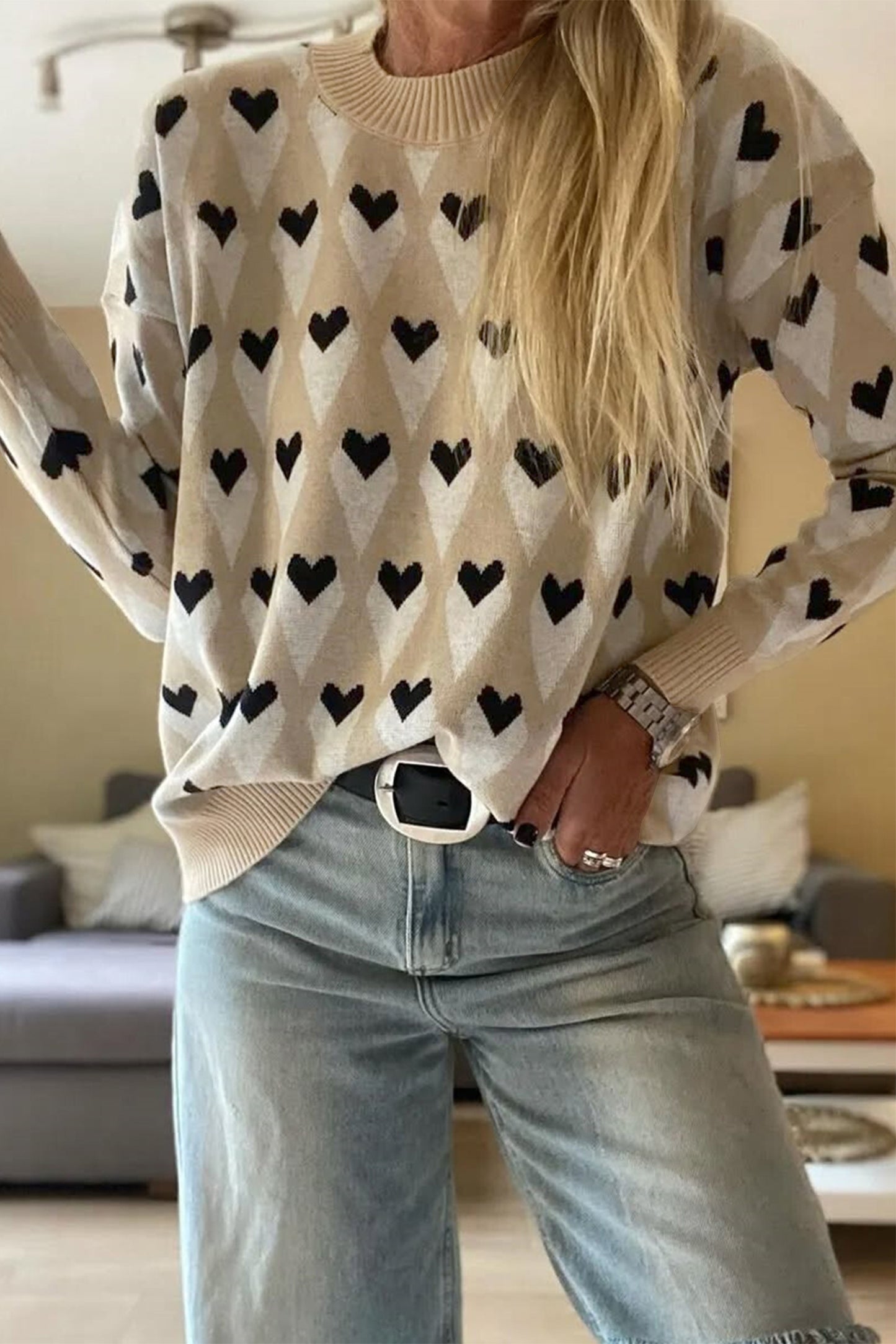 Woman wearing a beige geometric heart-print sweater with black heart details, styled with light-wash denim from The Pink Doxie Boutique.