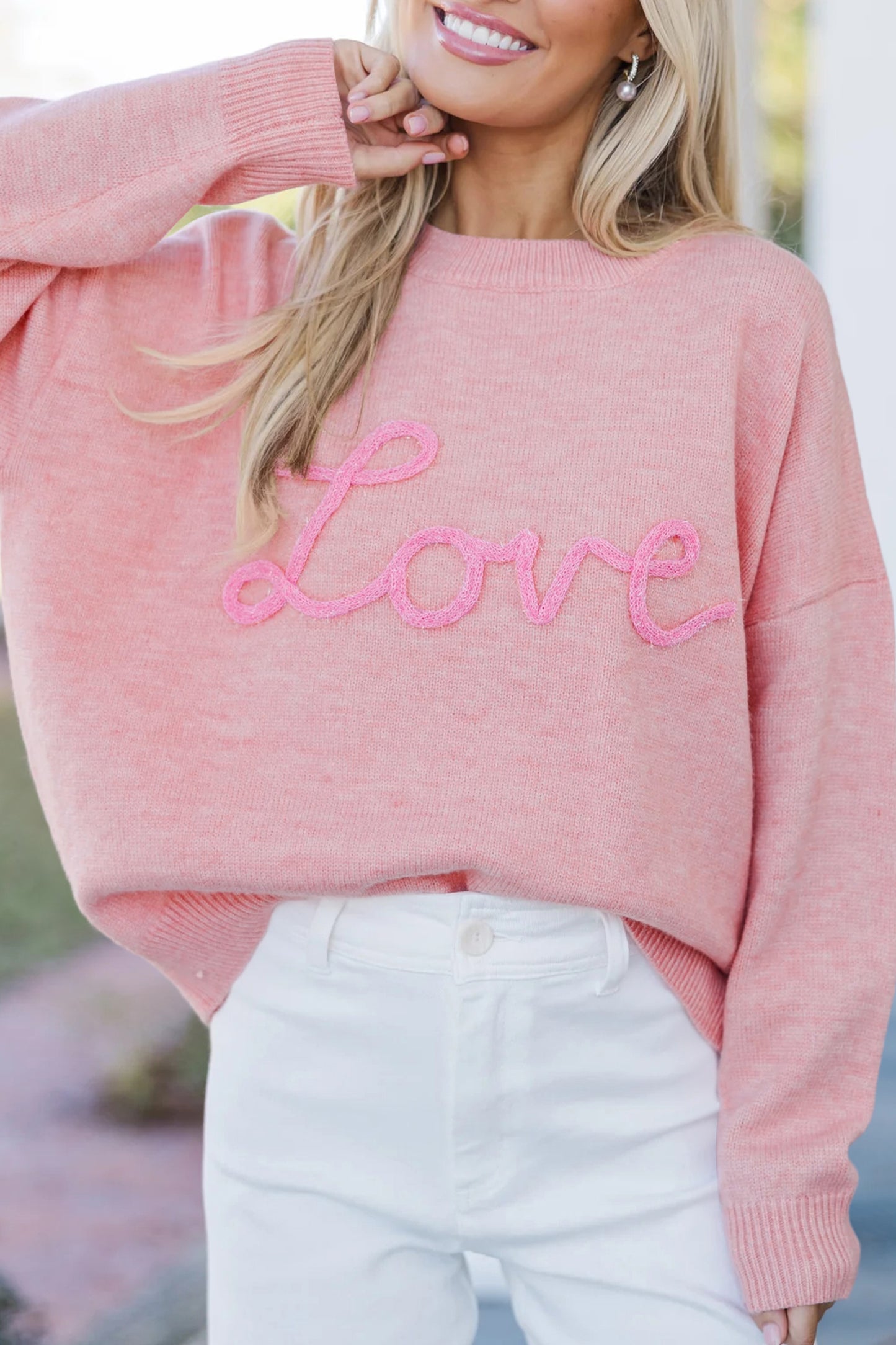Pink knit sweater with textured love script lettering styled with white jeans, photographed for The Pink Doxie Boutique.