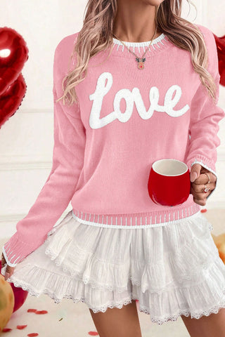 Pink knit sweater with white chenille “Love” lettering and contrast trim, styled with a white ruffled skirt from The Pink Doxie Boutique.