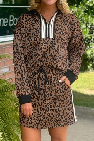 Woman wearing a leopard print two-piece set with quarter zip pullover top and matching skort with drawstring waist and pockets from The Pink Doxie Boutique.