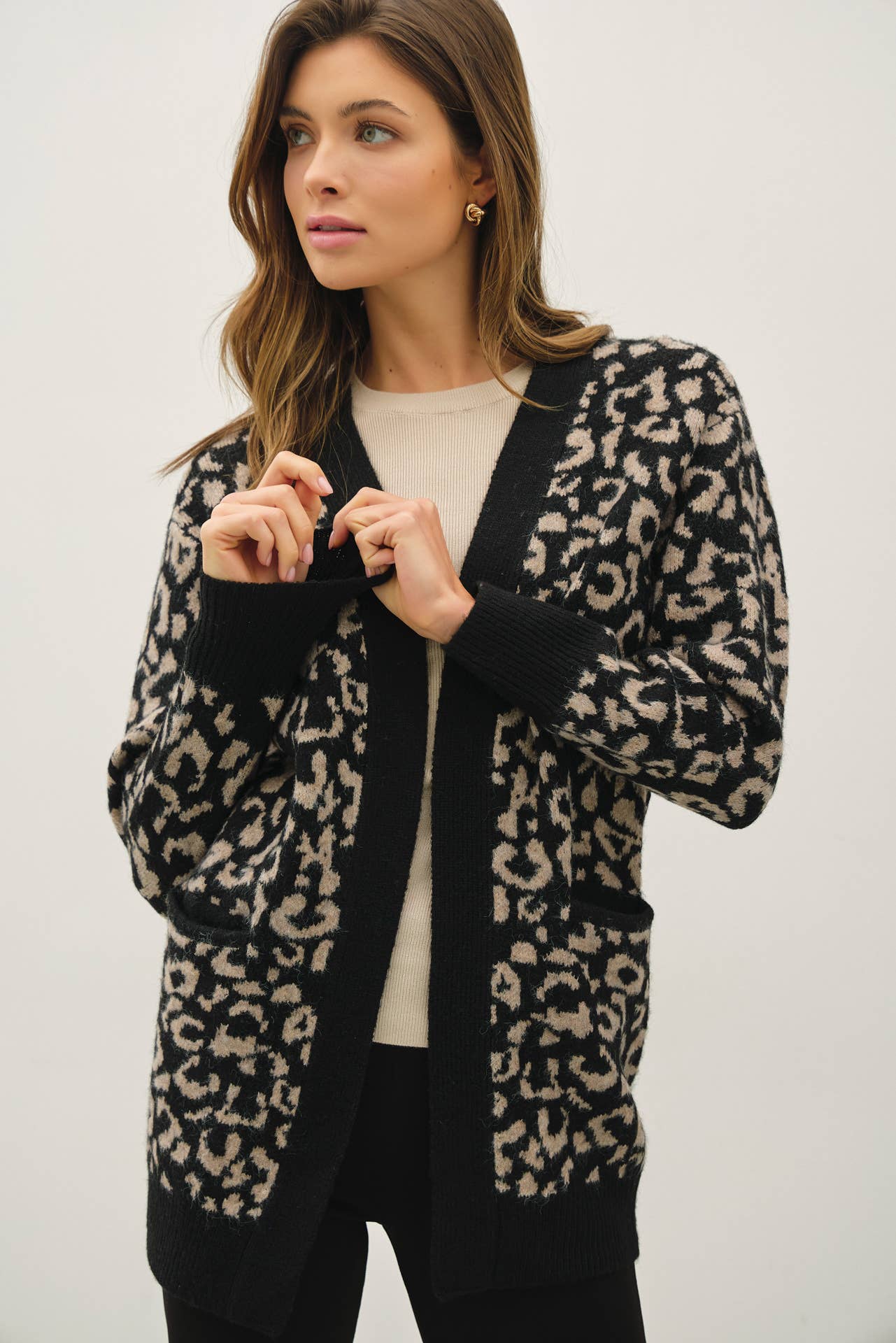 Woman wearing long leopard jacquard knit cardigan with front pockets.