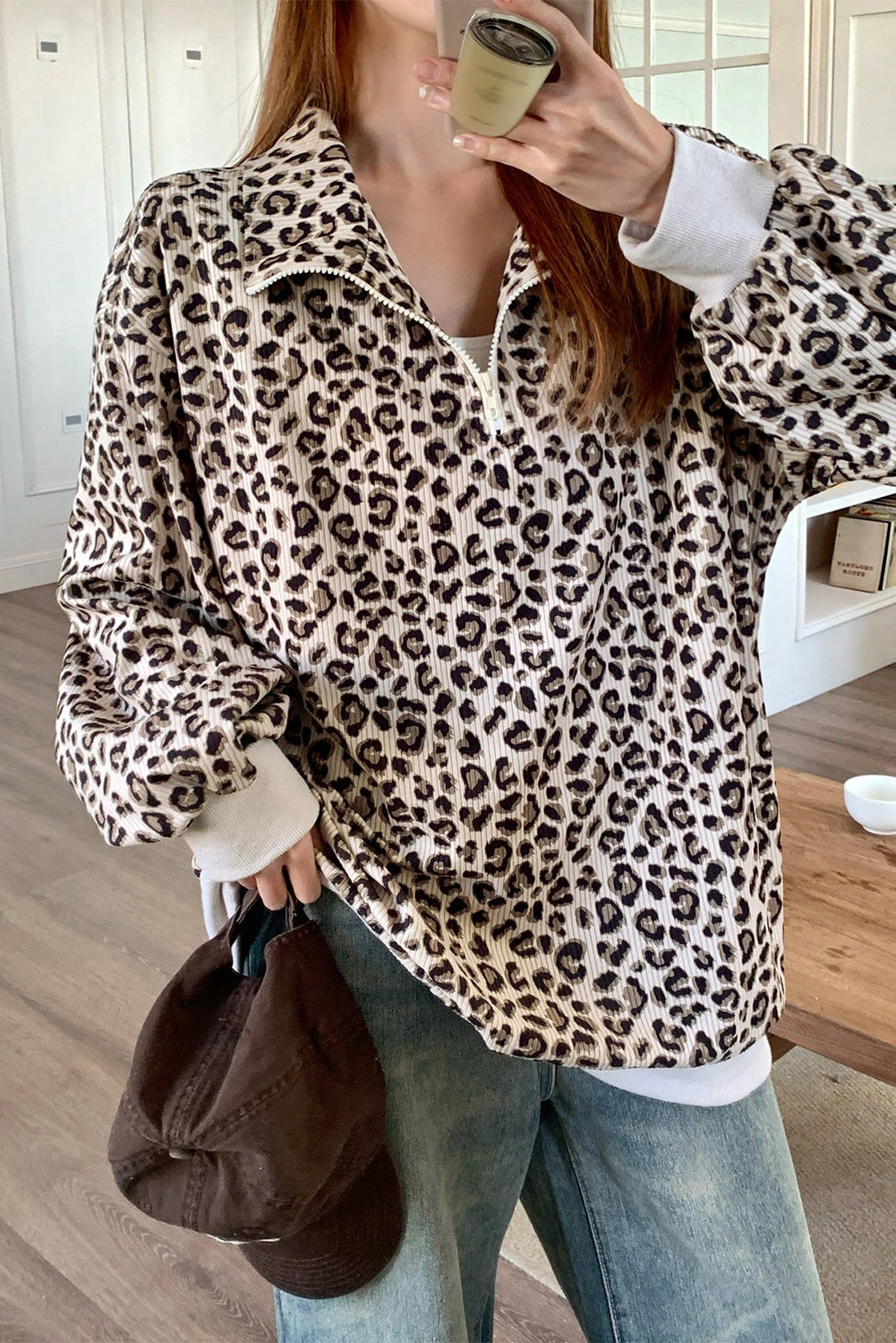 Woman wearing a leopard print quarter zip corduroy sweatshirt paired with relaxed denim jeans indoors.
