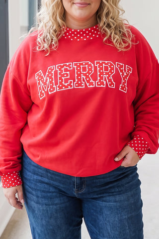 A plus-size model wearing a red pullover sweatshirt with a varsity-style polka dot "MERRY" graphic on the chest, a red-and-white polka dot mock-neck collar, and matching polka dot cuff trim, paired with dark-wash jeans.