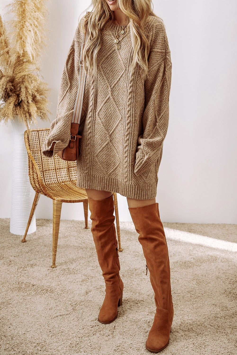 Woman wearing parchment cable knit sweater dress with drop shoulders, tan bag, and over-the-knee boots.