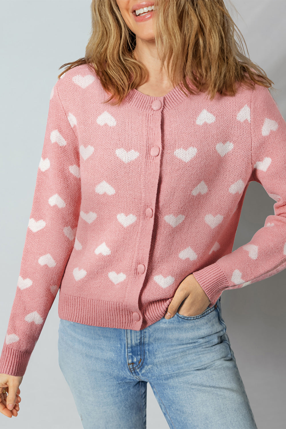 Woman wearing a light pink button-front cardigan with white heart patterns, styled casually with light blue jeans.