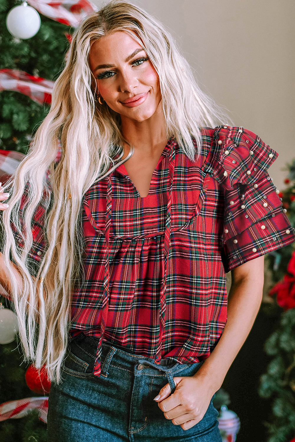 Woman wearing a red plaid short sleeve blouse with pearl embellishments and ruffled sleeves — festive holiday top from The Pink Doxie Boutique