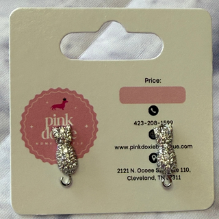 Silver sparkle cat-shaped earrings on a Pink Doxie card with contact information.