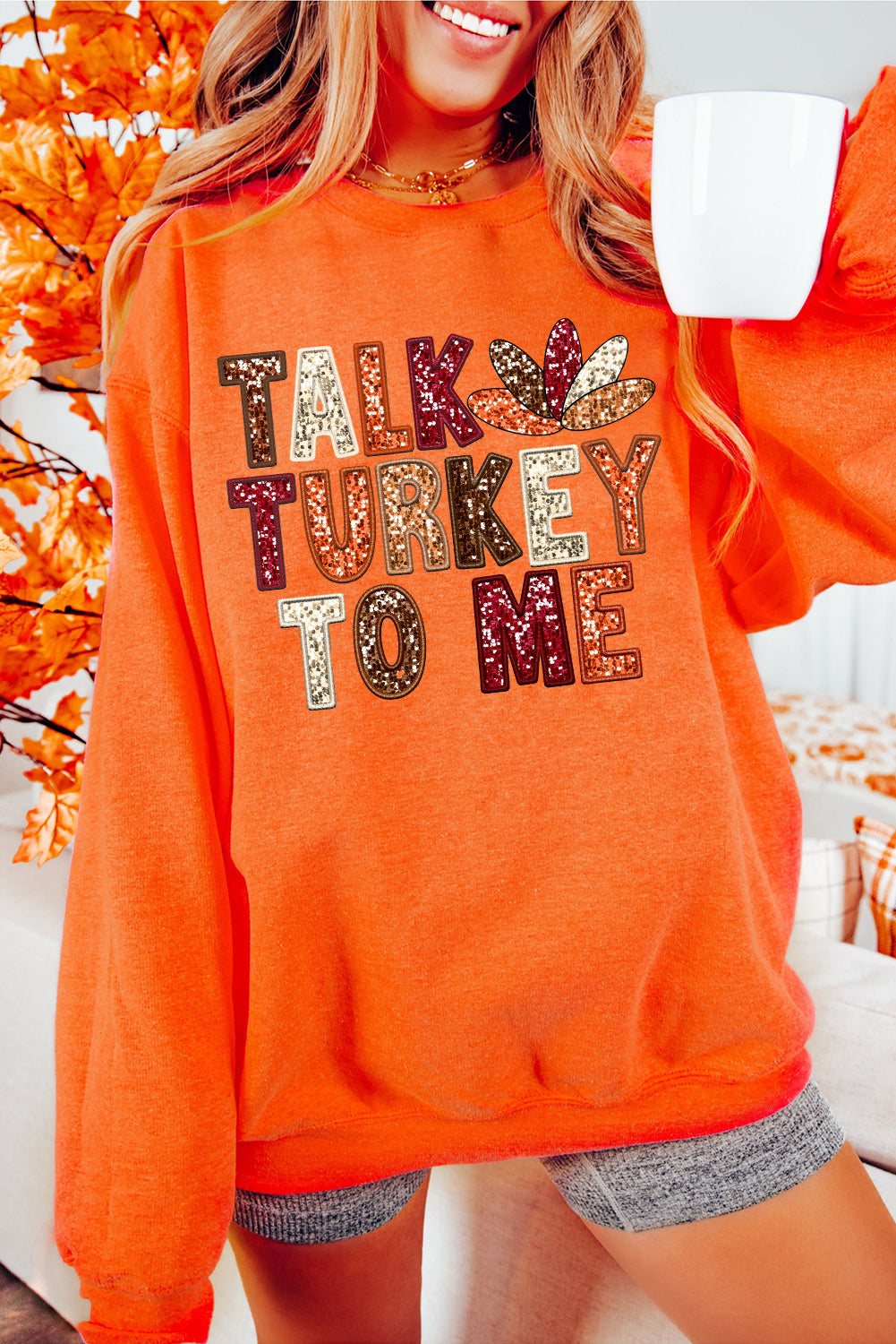 Woman wearing an orange sweatshirt with printed “Talk Turkey To Me” Thanksgiving graphic — cozy fall pullover from The Pink Doxie Boutique