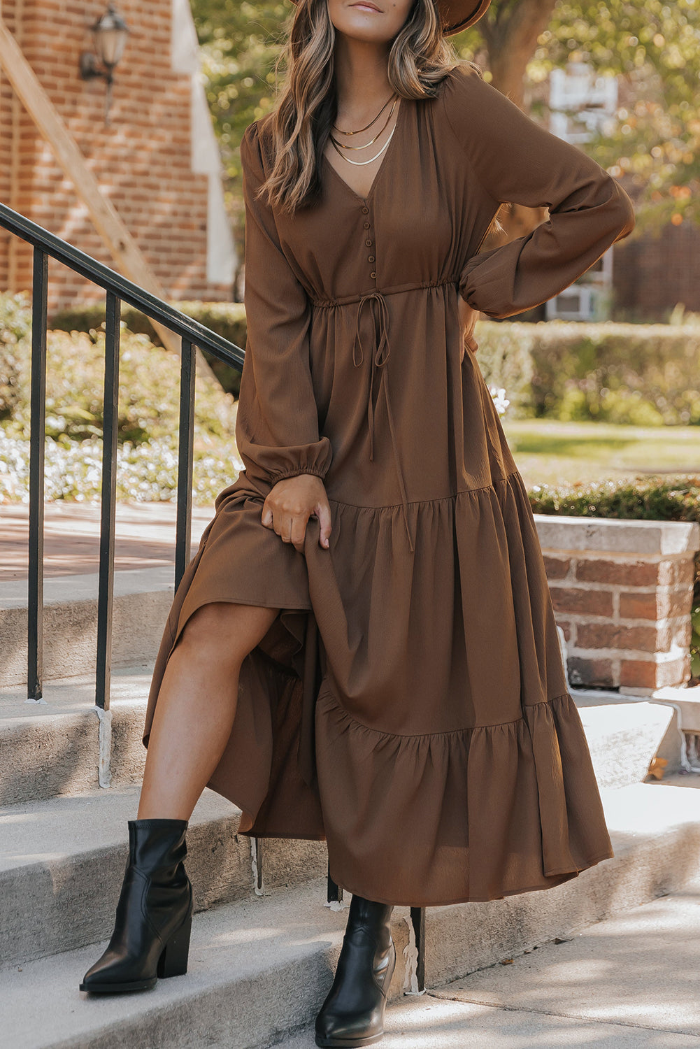 Model wearing a cocoa brown tiered long sleeve maxi dress with drawstring waist and V-neckline, styled with black boots.