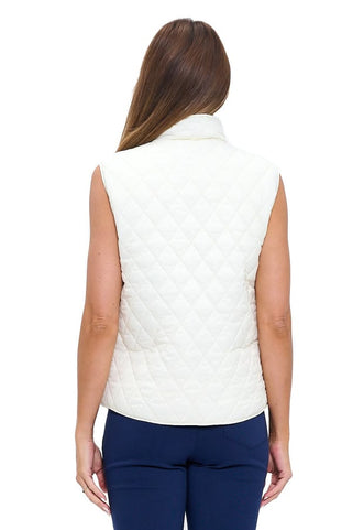 A woman wearing a cream white quilted sleeveless vest with a diamond quilt pattern, stand collar, full front zip, and two front patch pockets, styled over a white top with navy trousers.