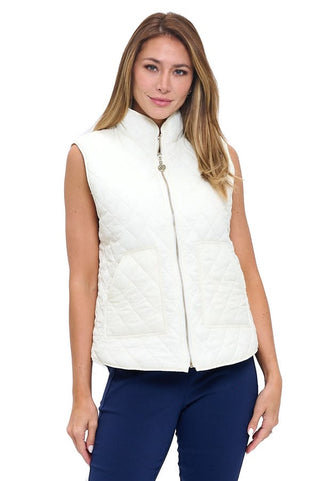 A woman wearing a cream white quilted sleeveless vest with a diamond quilt pattern, stand collar, full front zip, and two front patch pockets, styled over a white top with navy trousers.