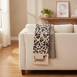 A cashmere blend scarf with a dachshund leopard print draped over a sofa.