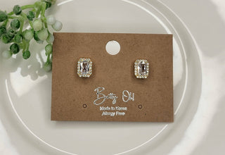 Rectangle cubic zirconia post earrings displayed on a kraft jewelry card with gold halo detail, shown at The Pink Doxie Boutique.